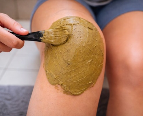 Heilerde wird mit einem Pinsel gleichmäßig als Auflage auf das Knie aufgetragen, Anwendung bei Gelenkbeschwerden oder Entzündung.