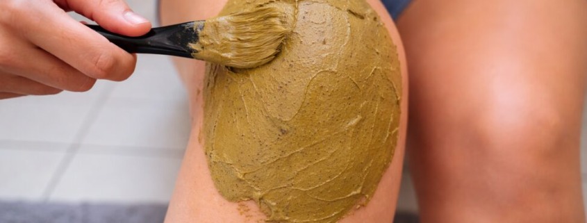 Heilerde wird mit einem Pinsel gleichmäßig als Auflage auf das Knie aufgetragen, Anwendung bei Gelenkbeschwerden oder Entzündung.