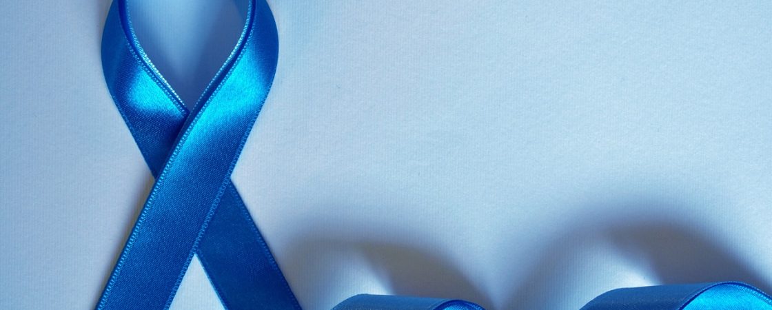 Blaues Schleifenband, zu einer symbolischen Schleife geformt, liegt auf einem hellblauen Hintergrund. Die Schleife steht für Bewusstsein und Unterstützung bestimmter Gesundheitskampagnen, wie beispielsweise Prostatakrebs- oder Darmkrebsvorsorge. Der restliche Teil des Bandes schlängelt sich sanft über die Oberfläche.