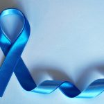 Blaues Schleifenband, zu einer symbolischen Schleife geformt, liegt auf einem hellblauen Hintergrund. Die Schleife steht für Bewusstsein und Unterstützung bestimmter Gesundheitskampagnen, wie beispielsweise Prostatakrebs- oder Darmkrebsvorsorge. Der restliche Teil des Bandes schlängelt sich sanft über die Oberfläche.