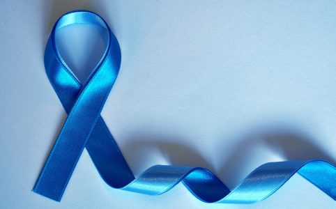 Blaues Schleifenband, zu einer symbolischen Schleife geformt, liegt auf einem hellblauen Hintergrund. Die Schleife steht für Bewusstsein und Unterstützung bestimmter Gesundheitskampagnen, wie beispielsweise Prostatakrebs- oder Darmkrebsvorsorge. Der restliche Teil des Bandes schlängelt sich sanft über die Oberfläche.