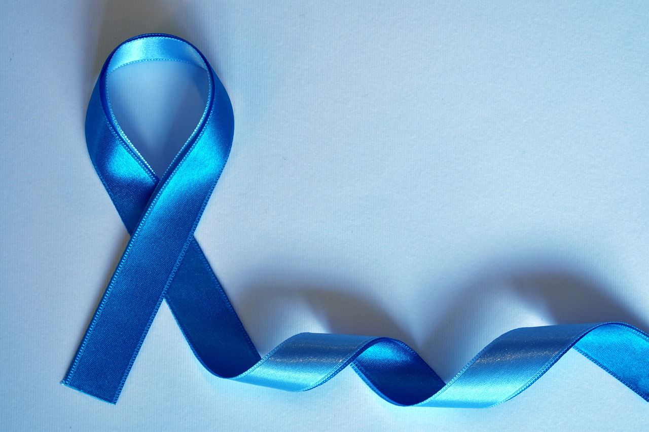 Blaues Schleifenband, zu einer symbolischen Schleife geformt, liegt auf einem hellblauen Hintergrund. Die Schleife steht für Bewusstsein und Unterstützung bestimmter Gesundheitskampagnen, wie beispielsweise Prostatakrebs- oder Darmkrebsvorsorge. Der restliche Teil des Bandes schlängelt sich sanft über die Oberfläche.
