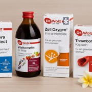 Dr. Wolz Produkte Darmflora plus, Vitalkomplex, Zell Oxygen und Thromboflow auf Holztisch mit Blüten dekoriert